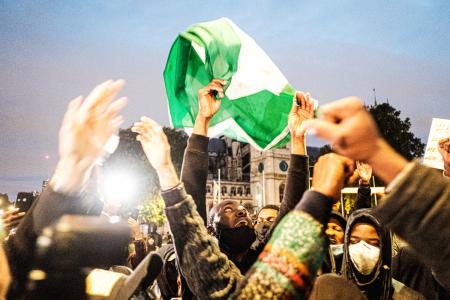 A crowd gathered to protest, with a person holding a Nigerian flag